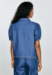 Denim takki, jossa on lyhennetty malli, puffatut lyhyet hihat, tavallinen kaulus ja näkyvä ompelu. Sininen väri ja sileä pinta.