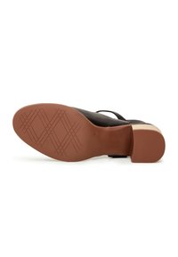 Chaussure à talon en cuir noir allongée sur le côté, montrant une semelle marron avec un motif de bande croisée et un talon bloc.