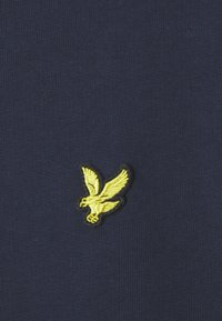 Tessuto blu navy con un dettagliato logo della aquila ricamato in giallo sul lato sinistro. Texture liscia con un sottile motivo a coste.