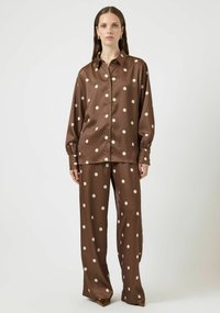 Brun satinbluse og matchende bukser, begge med store kremfargede polkadotter. Har spiss krage, knappelukking foran og lange ermer.