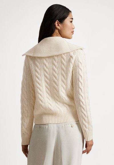 Pulover iz debele pletene tkanine v krem barvi, z rebrastim velikim ovratnikom, dolgimi rokavi in oprijetim spodnjim delom. Mehek, teksturiran material s podrobnimi vzorci.