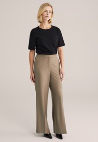 Čierny textúrovaný top s krátkym rukávom v kombinácii s béžovými širokými nohavicami s vysokým pásom. Modelka má na nohách čierne topánky s úzkou špičkou a minimálne doplnky.