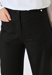 Pantaloni neri con una vestibilità su misura, dotati di due grandi tasche posteriori, chiusura con bottone e una texture di tessuto liscia e resistente.