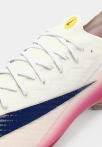 Calzature Nike con una tomaia bianca testurizzata, logo Swoosh blu e suola con gradiente rosa. Presentano lacci bianchi e un accento con logo giallo.