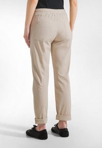 Pantalones beige con cintura elástica, puños enrollados y dos bolsillos traseros. El material parece suave con una textura lisa.