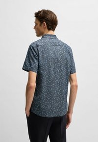 Camicetta a maniche corte in tessuto blu scuro con un motivo floreale e accenti blu chiaro. Design con colletto, orlo dritto e vestibilità rilassata.