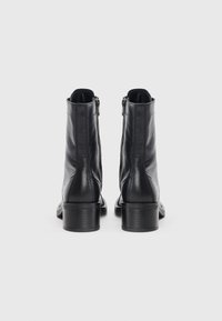 Schwarze Leder-Stiefeletten mit glatter Oberfläche, seitlichen Reißverschlüssen und einem klobigen Absatz, die ein minimalistisches Design ohne sichtbare Markenkennzeichnung aufweisen.