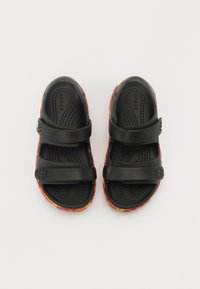 Černé sandály Crocs s dvěma nastavitelnými popruhy, texturovanou stélkou a vícebarevnou vzorovanou podrážkou s červenými, žlutými a oranžovými akcenty.