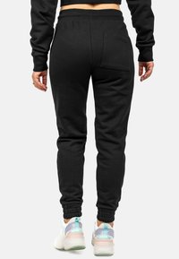 Zwarte joggers met een tapered fit, een elastische tailleband en boorden. Voorzien van een achterzak en gecombineerd met multicolore sneakers.