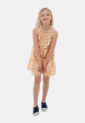 Robe orange clair avec un décolleté froncé, arborant un motif à pois orange et jaune. Associée à des chaussures en toile navy.