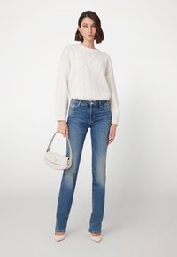 Lichtgewicht gebreid wit trui met textuurpatroon, blauwe denim jeans en een kleine witte handtas. Model draagt lichte hakken.