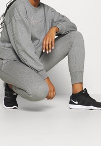 Szary dres Nike oraz zwężające się szare legginsy, zestawione z czarnymi butami sportowymi z białymi akcentami. Tkaniny wydają się miękkie i o ciekawej fakturze.