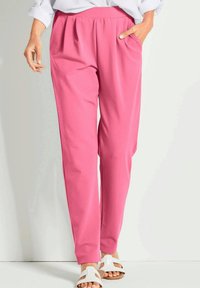 Roze broeken van zachte stof met een losse pasvorm, voorzien van zijzakken en een gladde tailleband, gecombineerd met witte sandalen.