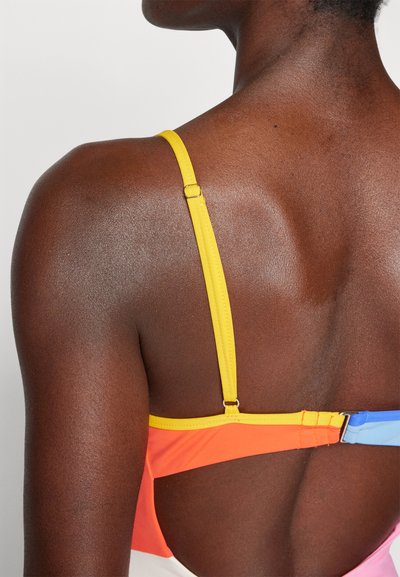 Farebný bikiny top má žlté popruhy s nastaviteľným kovovým zapínaním, kontrastné oranžové a modré panely a hladkú, textúrovanú tkaninu.