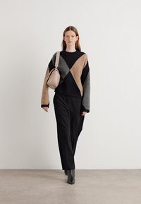 Suéter volumoso em blocos de cores preto, taupe e cinza, com mangas largas. Combinado com calças pretas largas e botas de tornozelo.