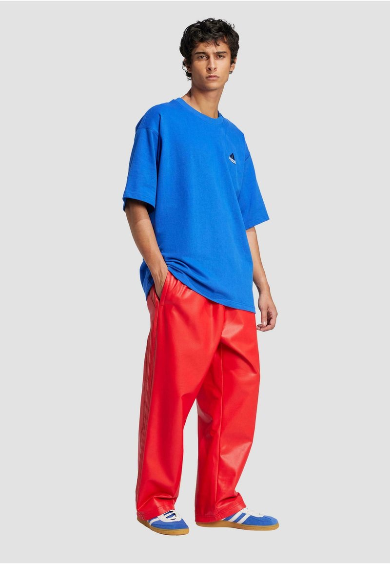 Blå oversized bomulds t-shirt med et lille brandlogo, parret med røde bukser i imiteret læder med bred ben. Hvide og blå sporty sko fuldender looket.