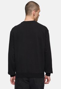 Felpa nera con collo rotondo, maniche lunghe, spalle scese e polsini a costine. Tessuto morbido con minimi dettagli di cucitura visibili.