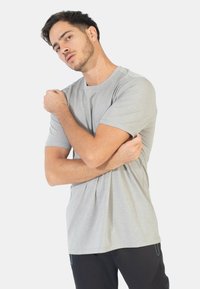 Grå kortærmet t-shirt med et tekstureret mønster og en afslappet pasform, båret med armene korslagt mod en ensfarvet hvid baggrund.