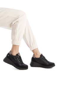 Zapatillas deportivas negras con una mezcla de cuero y ante, que presentan un detalle de cremallera, acentos texturizados y un diseño de suela gruesa.