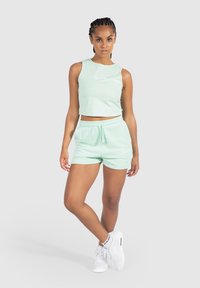 Top corto en verde menta y pantalones cortos a juego, hechos de una tela suave, con un corte relajado y una cinturilla elástica. Zapatillas blancas completan el look.