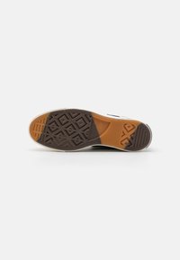 Semelle de chaussure avec grip en caoutchouc marron et orange, présentant des motifs géométriques et des sections texturées pour l'adhérence sur fond blanc.