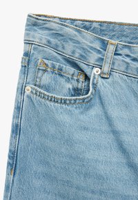 Jeans de mezclilla azul claro con un diseño clásico de cinco bolsillos, detalles de costura prominentes y una textura ligeramente deslavada.