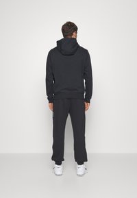 Sort hættetrøje med matchende joggers. Lavet af blødt materiale, har ribbede bærestykker og talje, med en diskret logo detalje på siden.