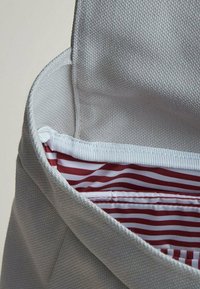 Borsa in tessuto grigia con una texture morbida, caratterizzata da una fodera interna a righe rosse e bianche e un bordo di chiusura bianco. Parte superiore aperta per rivelare l'interno.