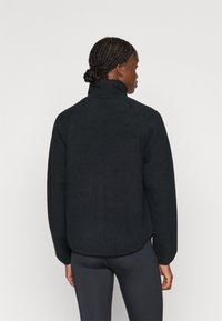 Jachetă din fleece neagră cu guler înalt și mâneci raglan. Material texturat, croială lejeră și un tiv curbat care se termină la șolduri.