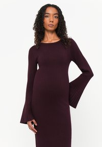 Abito a maglia viola a coste con maniche lunghe e svasate e scollatura rotonda; la silhouette aderente esalta la forma. Texture liscia e caldo.