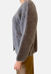 Grauer, flauschiger Pullover mit lockerer Passform, weitem Schnitt und weicher Textur. Kombiniert mit beigen Hosen, die ein schlichtes, entspanntes Design zeigen.