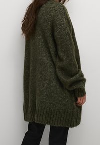 Ciemnozielony, oversize'owy sweter z dzianiny z prążkowanymi mankietami i dołem. Teksturowana tkanina o luźnym kroju i opadających ramionach.