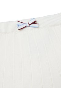 Geribbelde crèmekleurige stof heeft een decoratieve strik met blauwe en bordeauxrode strepen, wat detail toevoegt aan de tailleband. Soepele textuur overal.