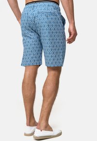 Shorts à motifs bleus avec un design en losange, fabriqués en tissu léger. Comprend une poche arrière et une taille élastique. Chaussures blanches à enfiler.