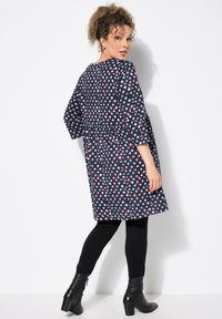Vestido azul marino de corte suelto, con un patrón de lunares blancos y rojos. Mangas largas y cintura ceñida. Combinado con leggings negros y botas de tobillo.