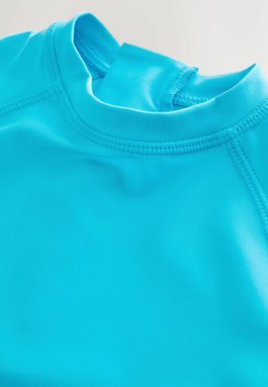 Turkos rashguard i mjukt, töjbart tyg; har en rundad halsringning och platta sömmar för komfort.