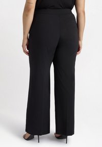 Svarta vida byxor med elastisk midja och sidfickor, slät textur och fåll som slutar strax ovanför ankeln.