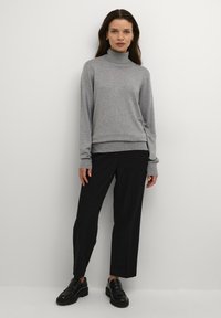 Grå strikket turtleneck sweater med lange ærmer og ribbet kant, parret med sorte skræddersyede bukser og sorte loafers.