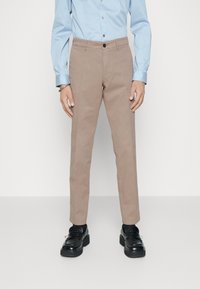 Beiga chinos i bomull, med rak benpassform och en enda knappstängning. Matchas med en ljusblå långärmad skjorta och svarta skor.