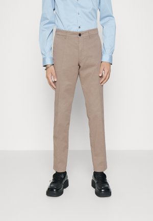 Chinos beiges en coton, avec une coupe droite et une fermeture à un bouton. Associés à une chemise à manches longues bleu clair et des chaussures noires.
