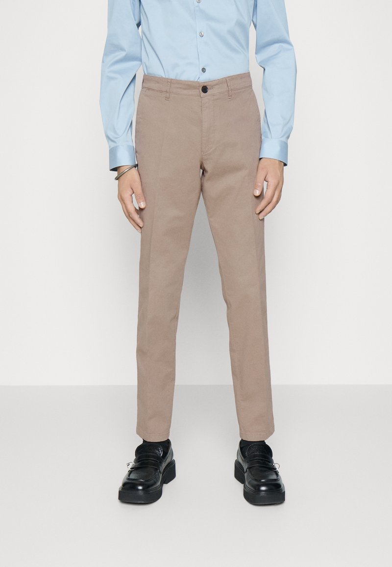 Beiga chinos i bomull, med rak benpassform och en enda knappstängning. Matchas med en ljusblå långärmad skjorta och svarta skor.