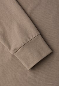 Langärmliges Kleidungsstück mit engem Bündchen, aus glattem, leichtem Stoff in einem sanften Taupe-Ton, mit einer dezenten gerippten Struktur.