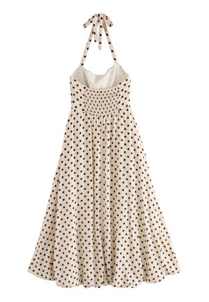 Beige zomerjurk met zwarte stippen, stof met gerimpelde buste en halterbandjes, vloeiende rok met plooien voor extra volume.
