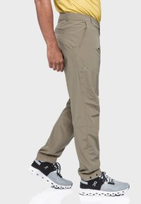 Beige, leichte Hosen im Slim-Fit-Schnitt. Enthält Taschen im Cargo-Stil und ein dezentes Markenlogo. Getragen mit grauen und schwarzen Laufschuhen.