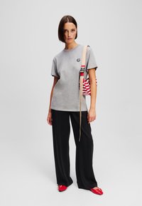 Grijze t-shirt met korte mouwen en een klein zwart logo, gecombineerd met zwarte broek met wijduitlopende pijpen en rode platte schoenen met een decoratieve gesp.