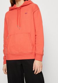 Coral sweatshirt with a hood, front kangaroo pocket, and drawstrings. Features a small Levi's logo, made of soft cotton blend fabric.