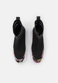 Pár černých tenisek ve stylu ponožek s bílými podešvemi a barevnými květinovými vzory na špičkách, zobrazené z ptačí perspektivy na bílém pozadí.