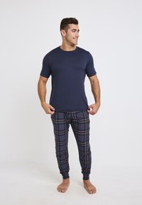 Marinblå t-shirt med kort ärm, matchad med rutig pyjamasbyxor i mörkblått, rött och beige, med slim fit och elastiska muddar.