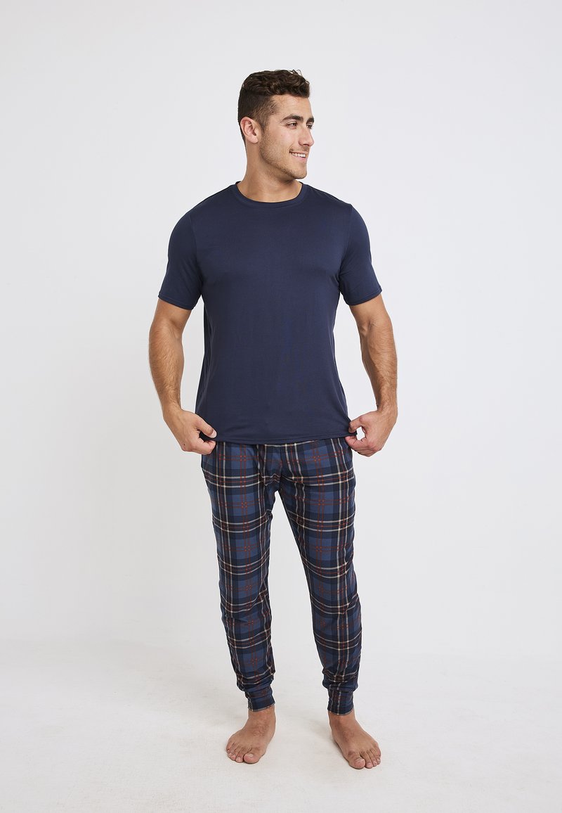 Marinblå t-shirt med kort ärm, matchad med rutig pyjamasbyxor i mörkblått, rött och beige, med slim fit och elastiska muddar.