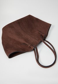 Brun ruskinds tote bag med matchende stropper, blød tekstur og et foldet design. Har kontraststing og dobbelte bånd på siden.